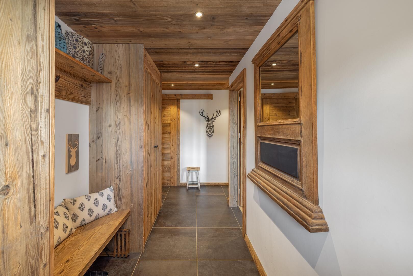 A hallway with wooden walls, a bench, a deer head decoration, and a window with a wooden frame.