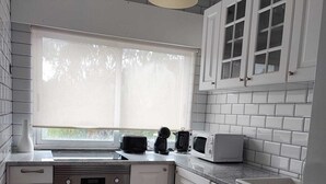 Een keuken met witte kasten, een inbouwoven, een magnetron en een raam met jaloezieën.