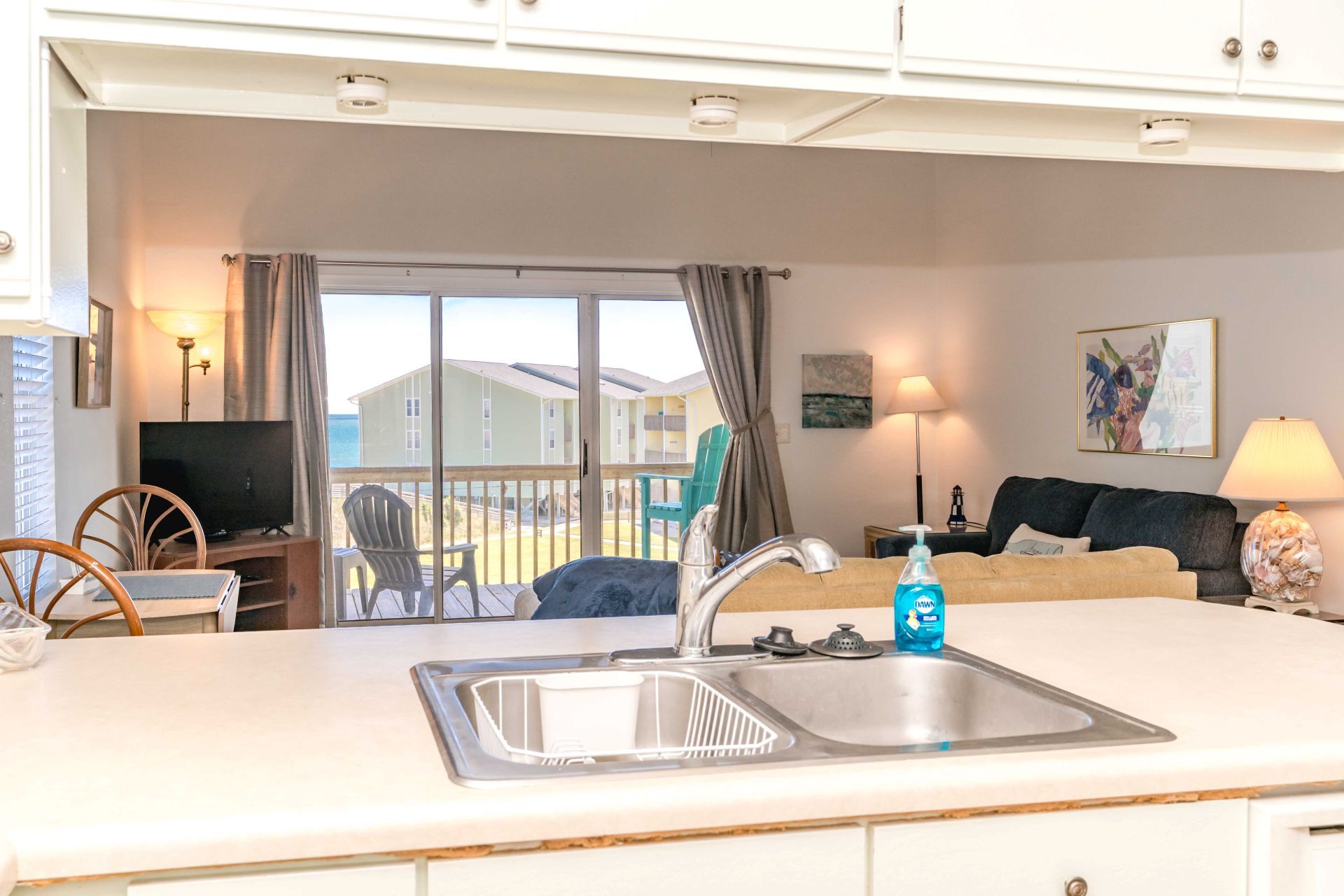 A kitchen with a sink, a dining area with chairs, a television, and a view of a building through a window.