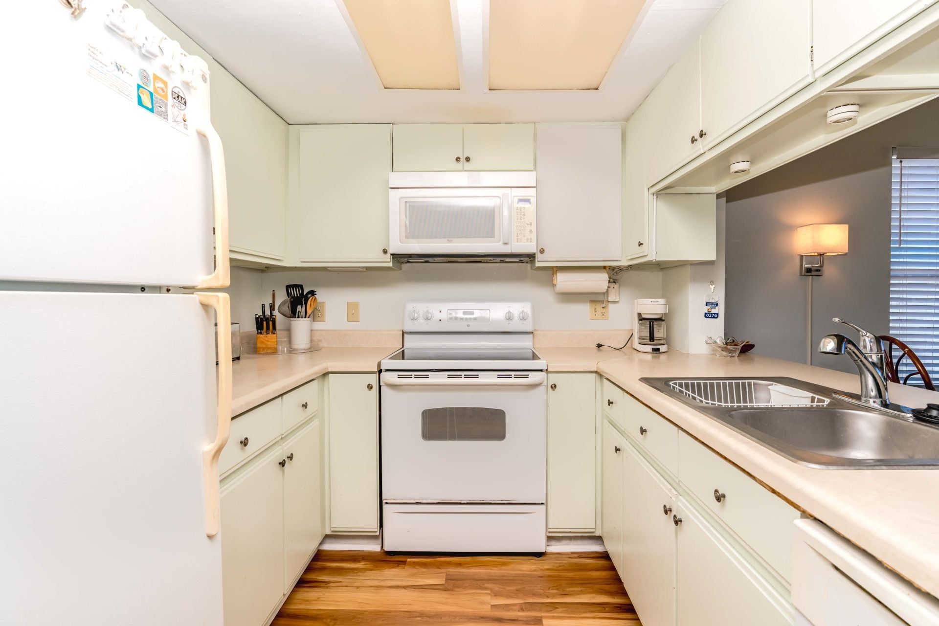 Une cuisine de taille réduite avec des meubles blancs, un four à micro-ondes, une cuisinière et un évier.