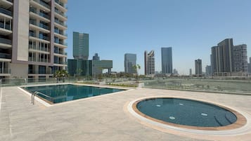 A rooftop pool area with a large rectangular pool and a smaller circular hot tub, surrounded by a tiled deck.