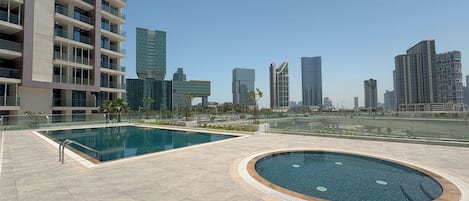 Un espace piscine aménagé sur le toit, comprenant une grande piscine rectangulaire et un petit jacuzzi circulaire, le tout entouré d’une terrasse carrelée.