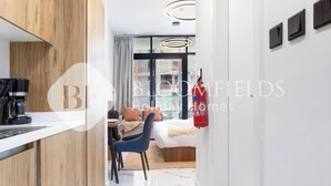 Een moderne hotelkamer met een houten accentmuur, een bureau met een koffiezetapparaat, een bed met een blauwe stoel, en een brandblusser aan de muur.