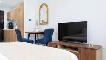 A hotel room with a bed, a TV, a desk with two chairs, a mirror, and a kitchenette.