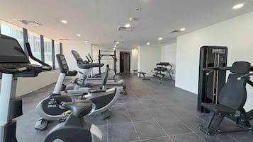 A modern gym with various cardio machines, weightlifting equipment, and a bench.