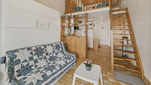 A cozy living room with a wooden staircase leading to a loft bedroom, a white sofa, and a small table with a plant. - 50 m from the beach – apart for 2 adults / 3 children (Longeville-sur-Mer)