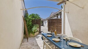Un patio exterior estrecho con una mesa lista para comer, rodeado de muros blancos y una valla de madera.