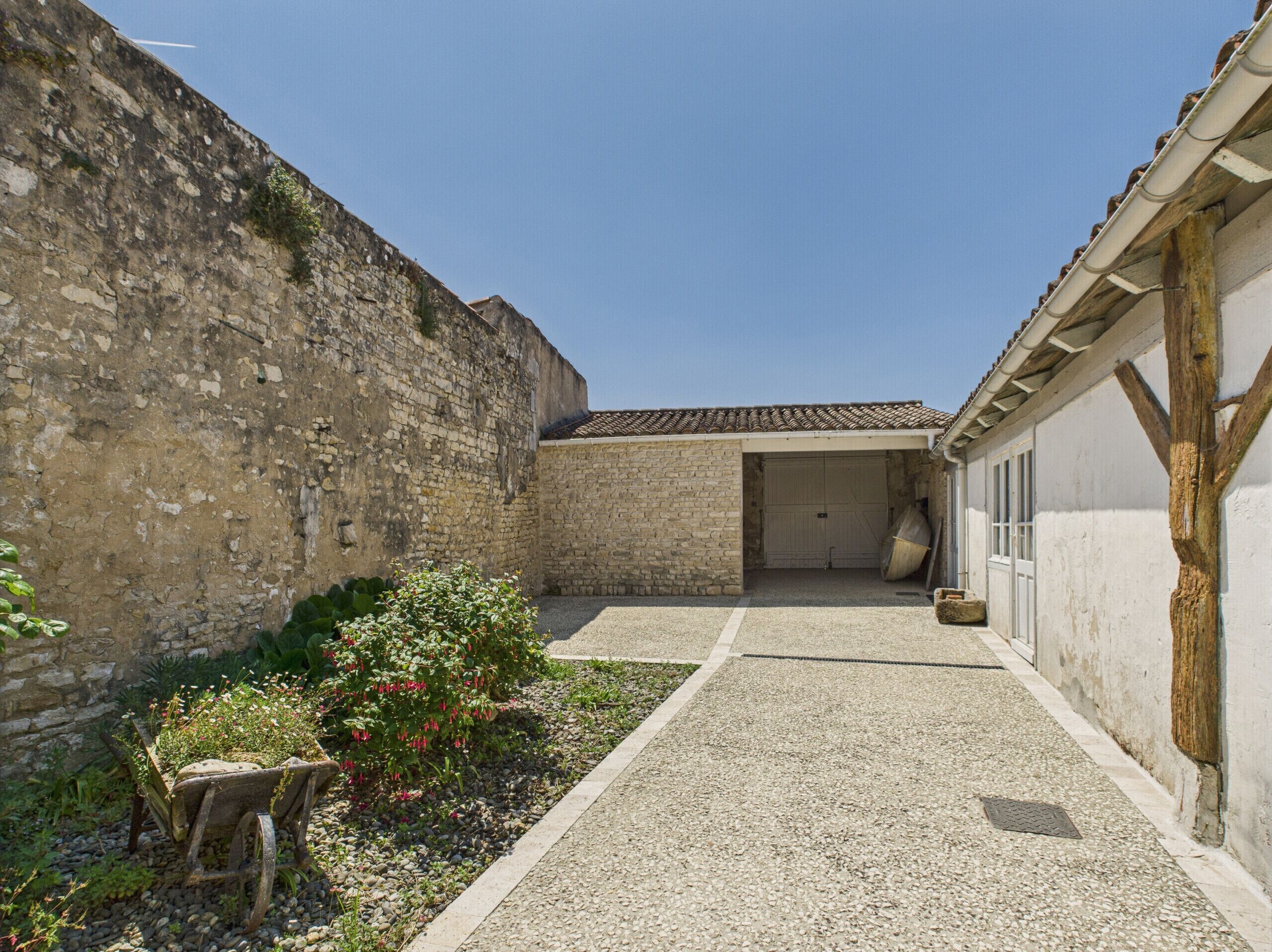A courtyard with a stone wall, a gravel path, and a building with a tiled roof.