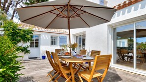 A wooden table with chairs and an umbrella in a patio area with a tiled floor and potted plants. - Heated pool, 800 m from the beach, villa for 8 (Noirmoutier-en-l´Ile)