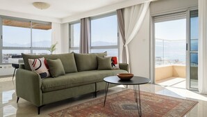 Ein modernes Wohnzimmer mit einem grünen Sofa, einem runden Tisch und Meerblick durch große Fenster.