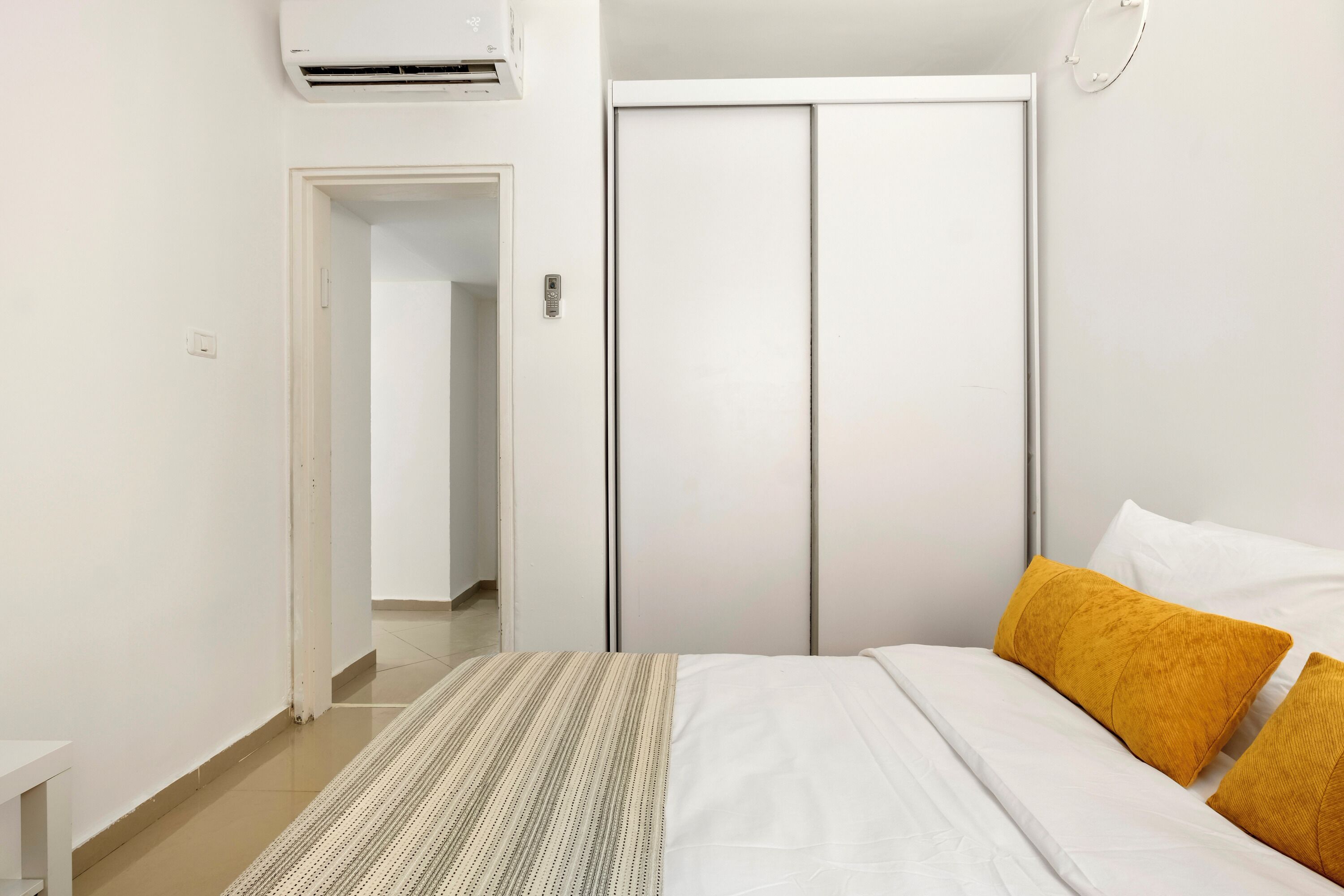 A bedroom with a bed, white bedding, a striped rug, and a wardrobe.