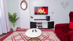 A living room with a flat-screen TV displaying a fireplace, a red sofa, a white coffee table, and a potted plant. - White House (Nairobi)