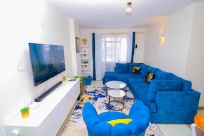 A modern living room with a blue sofa, a flat-screen TV, and a coffee table. - White House (Nairobi)