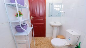 A compact bathroom with a white toilet, a pedestal sink, a red door, and a white tiled floor. - White House (Nairobi)
