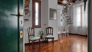 A room with wooden flooring, a spiral staircase, a green door, and two chairs.