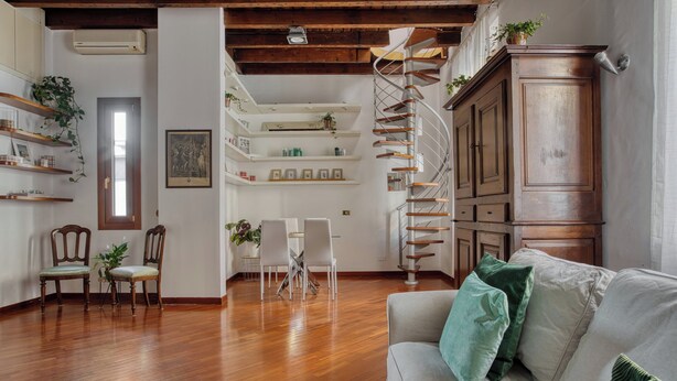 A living room with a wooden floor, a sofa with green cushions, a dining area with chairs and a table, and a spiral staircase.