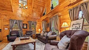 Ein gemütliches Cabin-Interieur mit Holzwänden, einem Ledersessel, einer Couch, einem Couchtisch und einem Schild mit der Aufschrift 'forever grateful'.