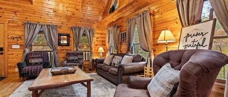 A cozy cabin interior with wooden walls, a leather armchair, a sofa, a coffee table, and a sign that reads 'forever grateful.'