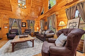 A cozy cabin interior with wooden walls, a leather armchair, a sofa, a coffee table, and a sign that reads 'forever grateful.'
