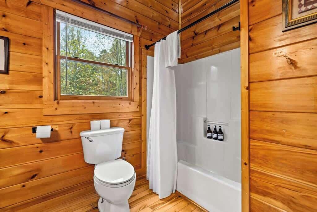 A wooden cabin bathroom with a toilet, a shower, and a window.