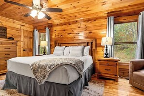 Une chambre à coucher dans une cabane en bois, avec un lit, une table de chevet, une commode et un ventilateur de plafond.