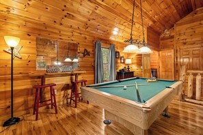 Un intérieur en bois agrémenté d’une table de billard, de tabourets de bar et de luminaires suspendus.