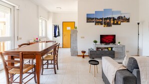 Een moderne woonkamer met een eethoek, een bank, een televisie en een kunstwerk van een stadsgezicht aan de muur.