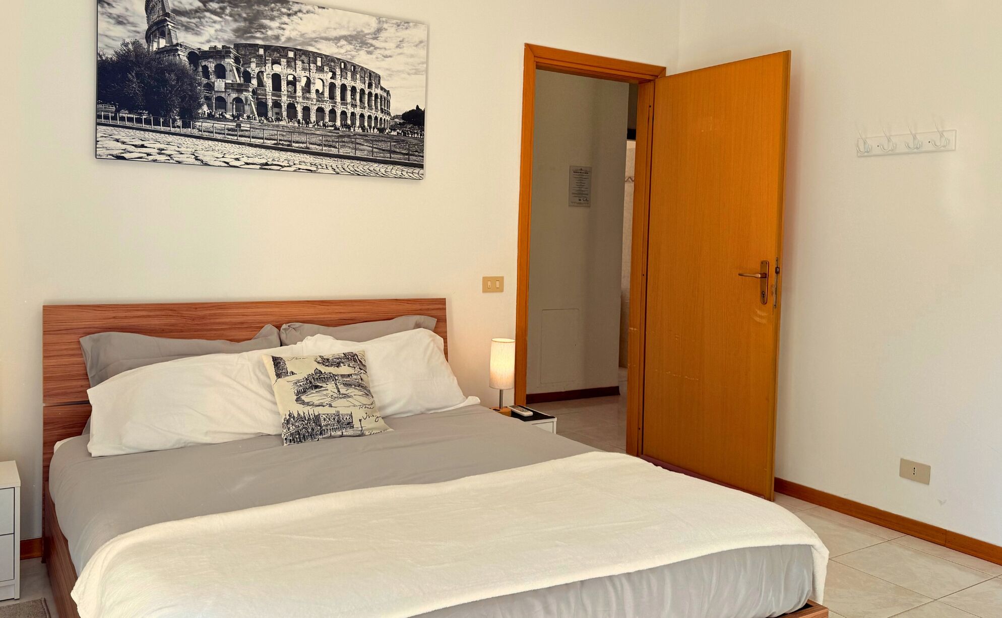 A hotel room with a bed, a nightstand, a lamp, a door, and a framed picture on the wall.
