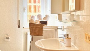 Een badkamer met een witte wastafel, een glazen plank en een rieten mand met handdoeken.