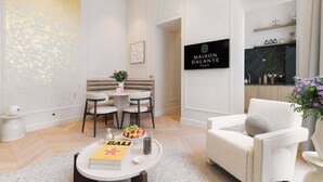 A modern living room with a dining area, a sofa, a coffee table with a book and a bowl of fruit, and a sign for Maison Galante Paris.