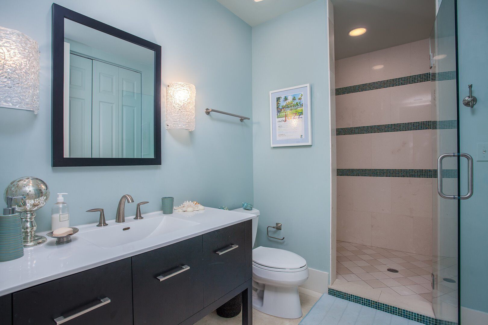A bathroom with a large mirror, two sinks, a toilet, and a glass-enclosed shower.