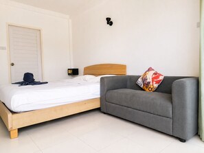 A bedroom with a bed, a grey sofa, a colorful pillow, a wall-mounted light, and a door. - K2 Seaside Suites (Pattaya)