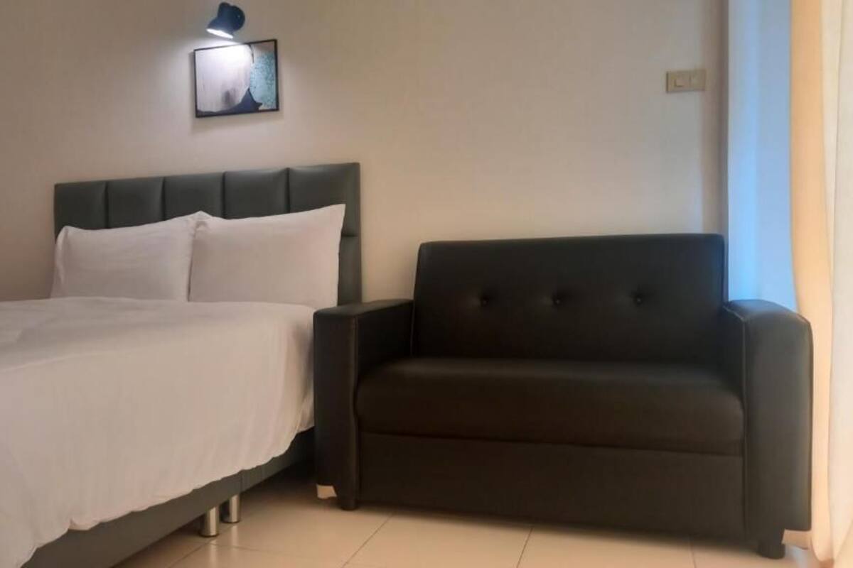 A bedroom with a bed, a dark-colored sofa, and a wall-mounted light fixture.
