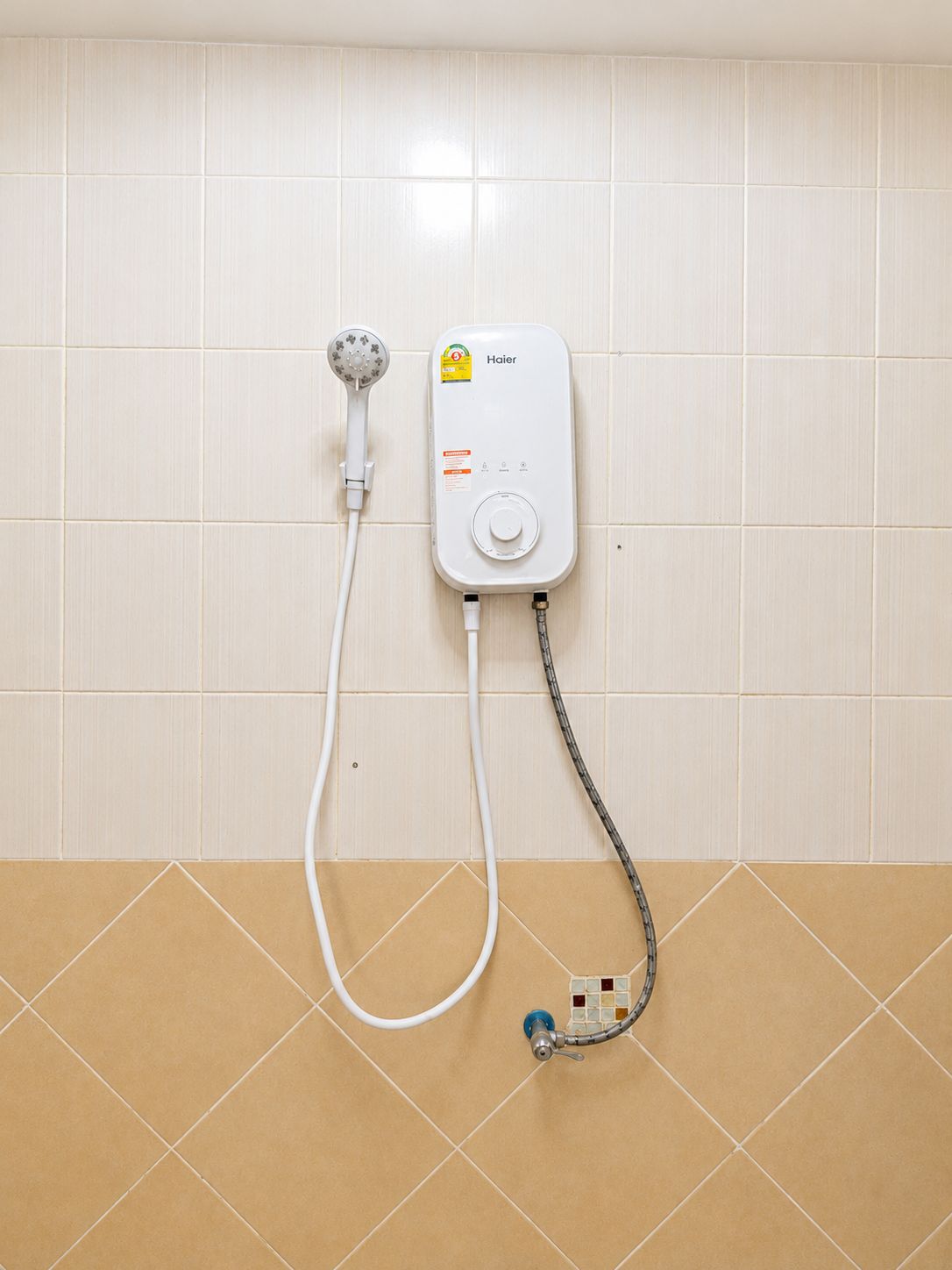 Un calentador de agua Haier blanco montado en una pared con baldosas color beige.
