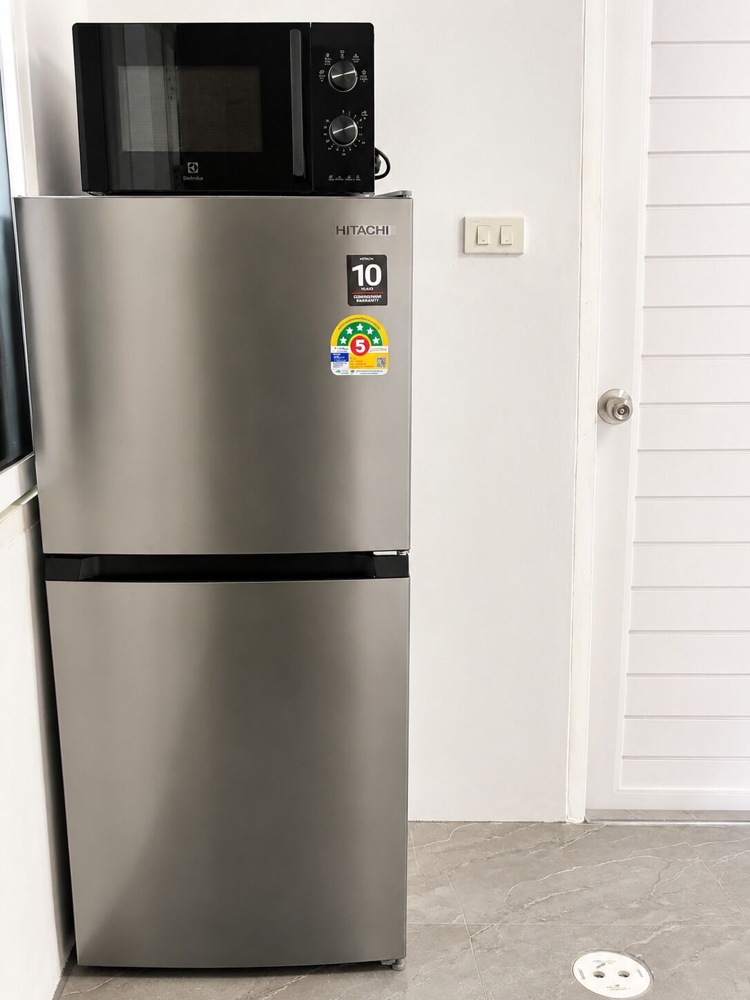 A stainless steel refrigerator with a microwave on top, a 10-year warranty sticker, and a 5-star energy efficiency rating.