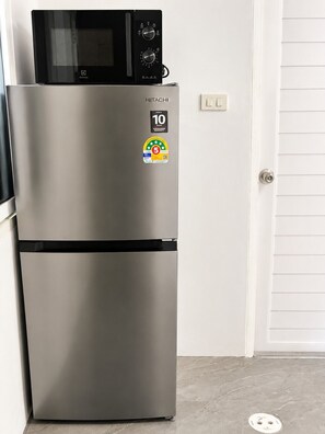A stainless steel refrigerator with a microwave on top, a 10-year warranty sticker, and a 5-star energy efficiency rating. - K2 Seaside Suites (Pattaya)