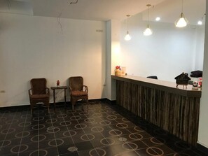 Ein Empfangsbereich mit zwei Korbstühlen, einem kleinen Tisch und einer Theke mit Holzverkleidung.