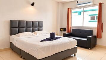 A hotel room with a bed, a sofa, an air conditioning unit, and a window with curtains.