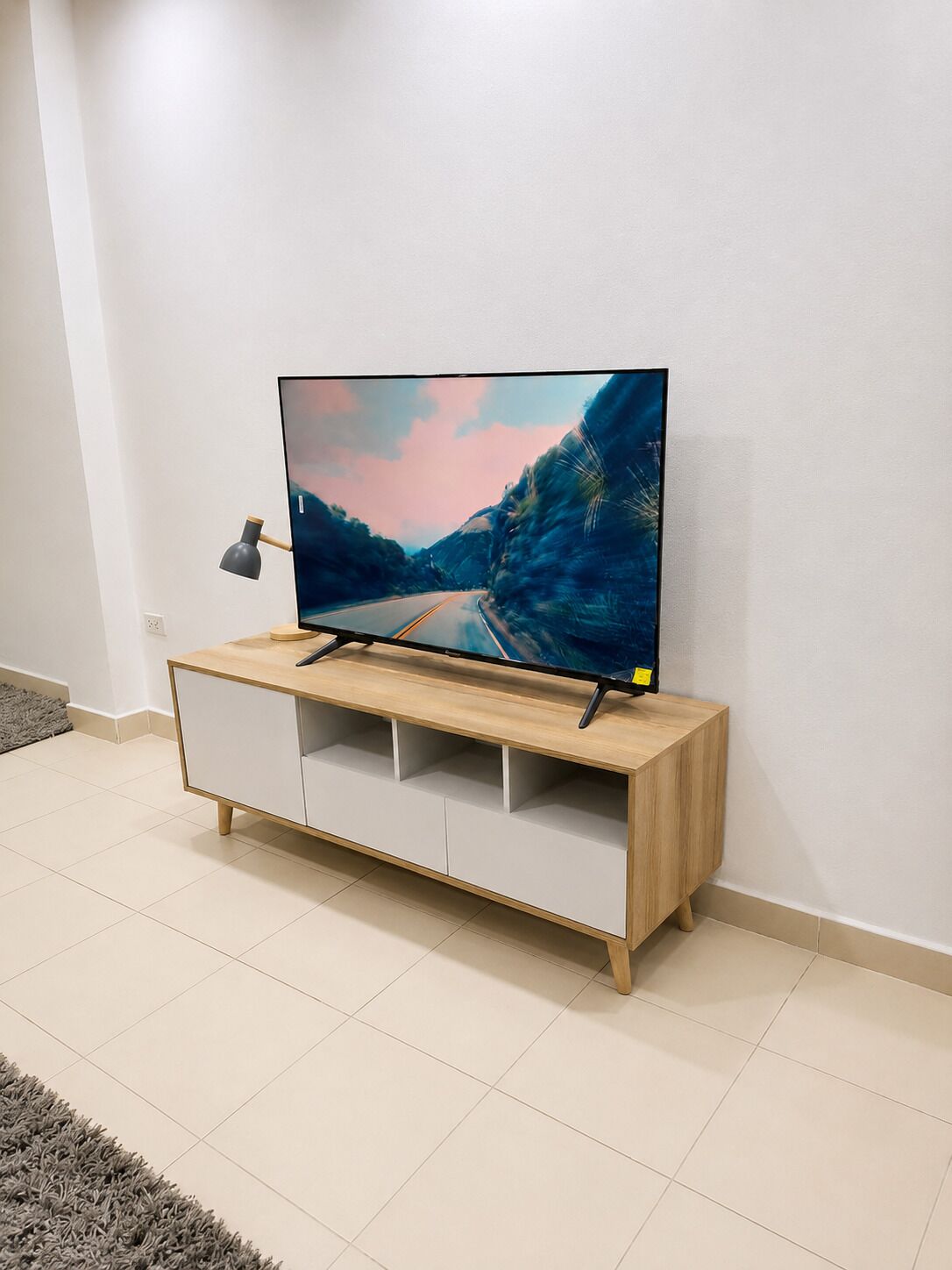 A flat-screen TV on a wooden TV stand with a minimalist design, placed against a plain wall.