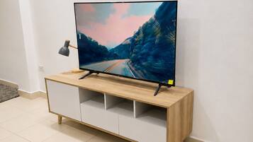 A flat-screen TV on a wooden TV stand with a minimalist design, placed against a plain wall.