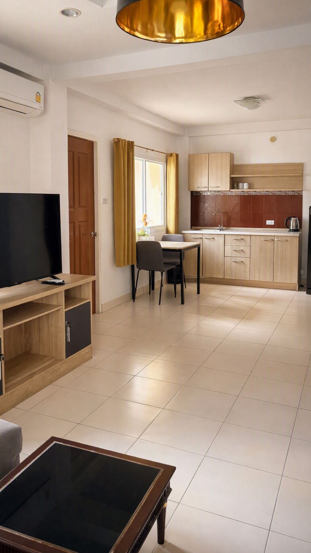 Ein modernes Wohnzimmer mit Fernseher, einem Glastisch und einem Essbereich mit Tisch und Stühlen.