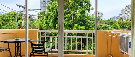 Un balcón con mesa y sillas, vista a un paisaje urbano y un edificio al fondo.