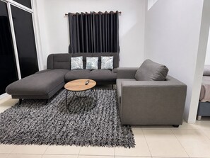 A modern living room with a grey sectional sofa, a round coffee table, and a grey rug. - K2 Seaside Suites (Pattaya)