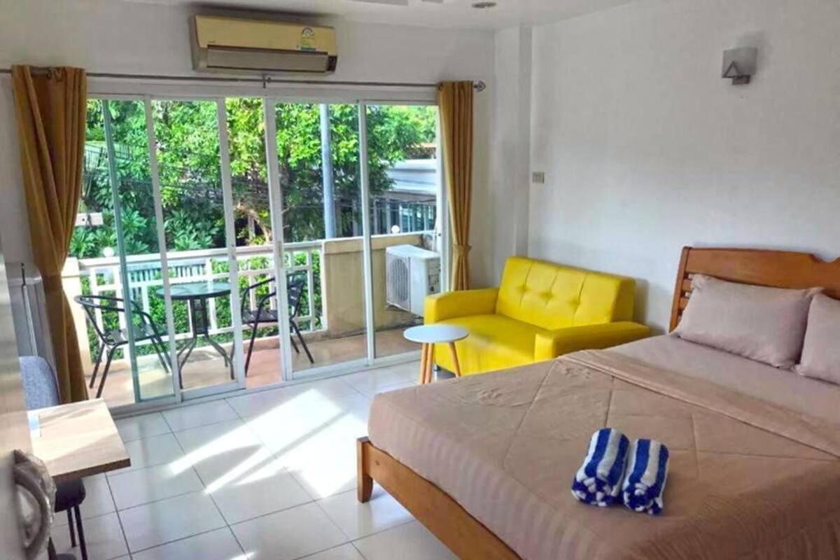 A hotel room with a bed, a yellow sofa, a small table, and a balcony with a table and chairs.