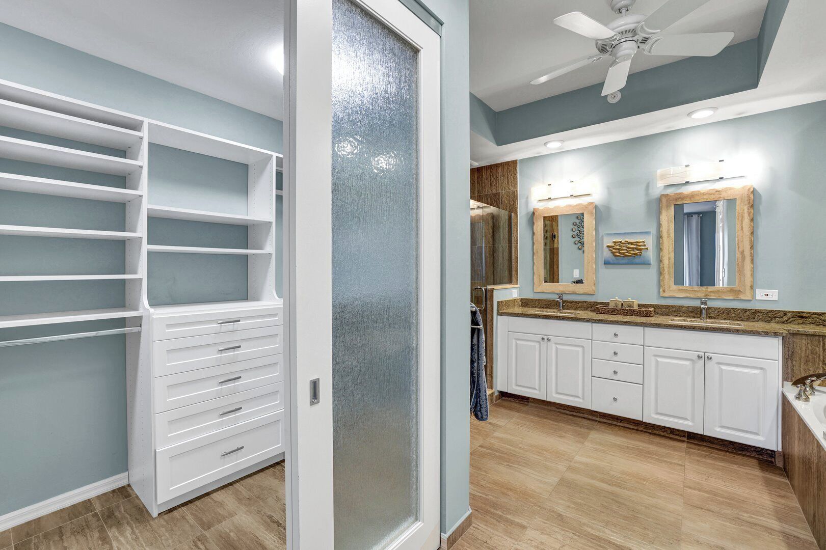 A modern bathroom with a walk-in closet, a vanity with a granite countertop, and a ceiling fan.