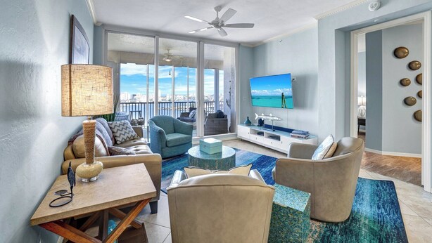 A spacious living room with a large TV, comfortable seating, a dining area, and a balcony with a view. - REGATTA - ENJOY GULF AND BAY VIEWS! (Naples)