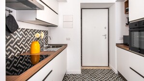 A compact kitchen with a modern design, featuring a black and white patterned backsplash, a wooden countertop, and a small yellow vase.