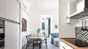 A modern kitchen with a dining area, featuring a herringbone-patterned floor, a dining table with chairs, a sofa, and a kitchen counter.