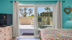 A hotel room with a bed, a dresser, a television, and a sliding glass door leading to a balcony with a table and chairs. - Oceanfront Ground Floor Condo Steps From Private Beach Access! (St. Augustine)