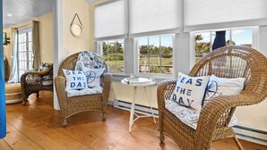 A room with wicker chairs, a small round table, and large windows with blinds. - Charming Seaside Cottage  Sleeps 9 with WiFi, AC, 2 Min Walk to a Private Beach (Sandwich)